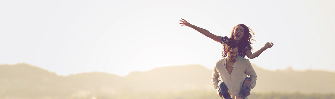 A woman smiles piggy backing on her proud husband's back with her arms stretched out after couples therapy. 