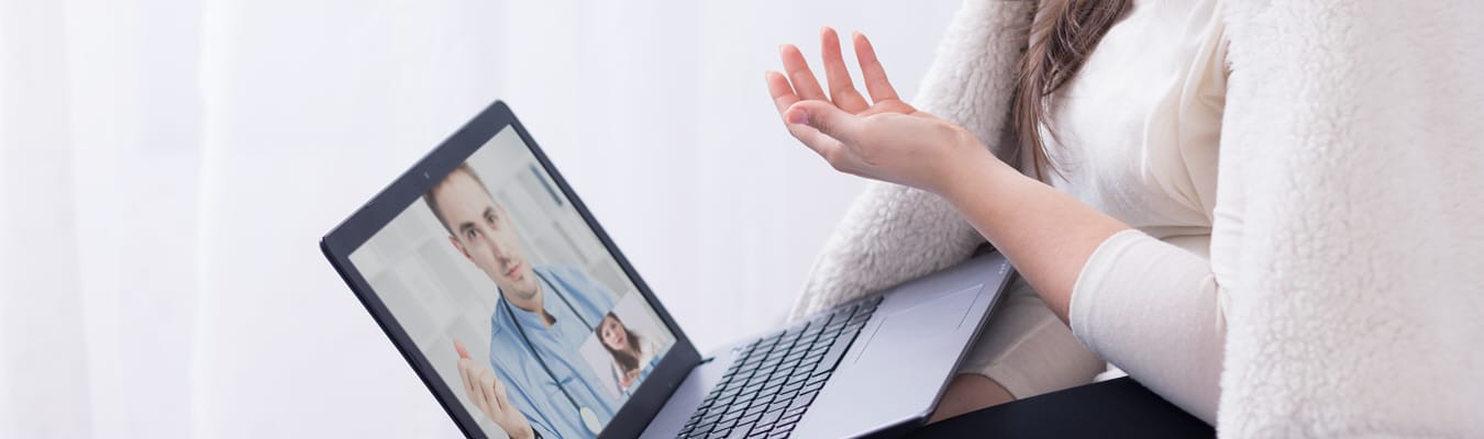 A psychologist has her laptop open and is doing therapy with a patient over video. 