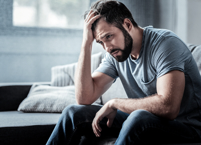 A handsome young man sits on his couch stressed, putting his right hand through his hair in dismay. No one gets him. 