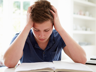 A studious male teen sits at his desk with his notebook open anxious and stressed. He can't concentrate on the assignment. 