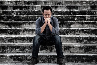 A man sits somber on the stairs with his hands covering his mouth in shock and disbelief. 