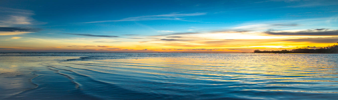 Small waves pass through the ocean water during sunset. 